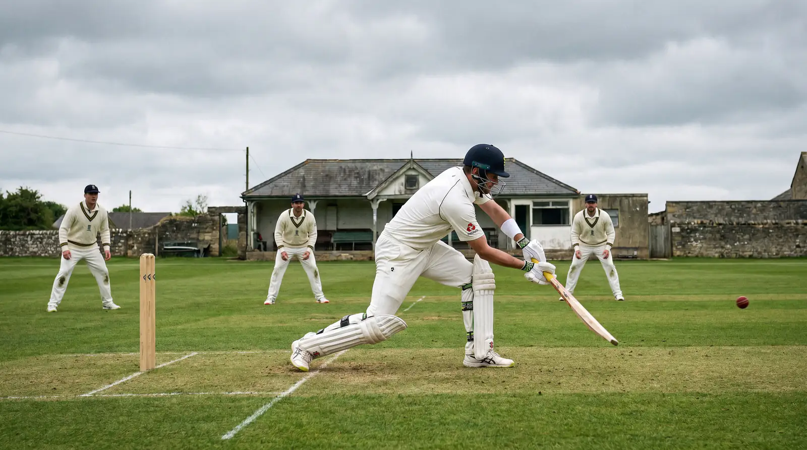 Batsman playing a defensive shot close to the body on a seaming green pitch in English conditions