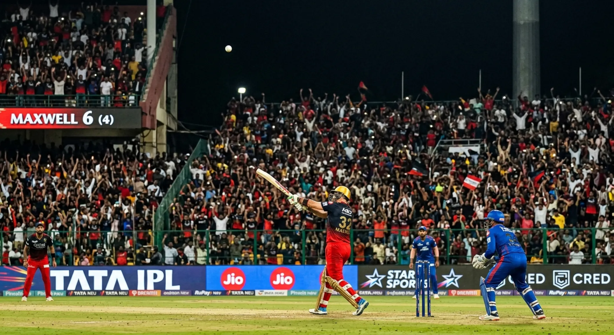 Cricket batsman smashing a six into the crowd during the death overs of a floodlit T20 match