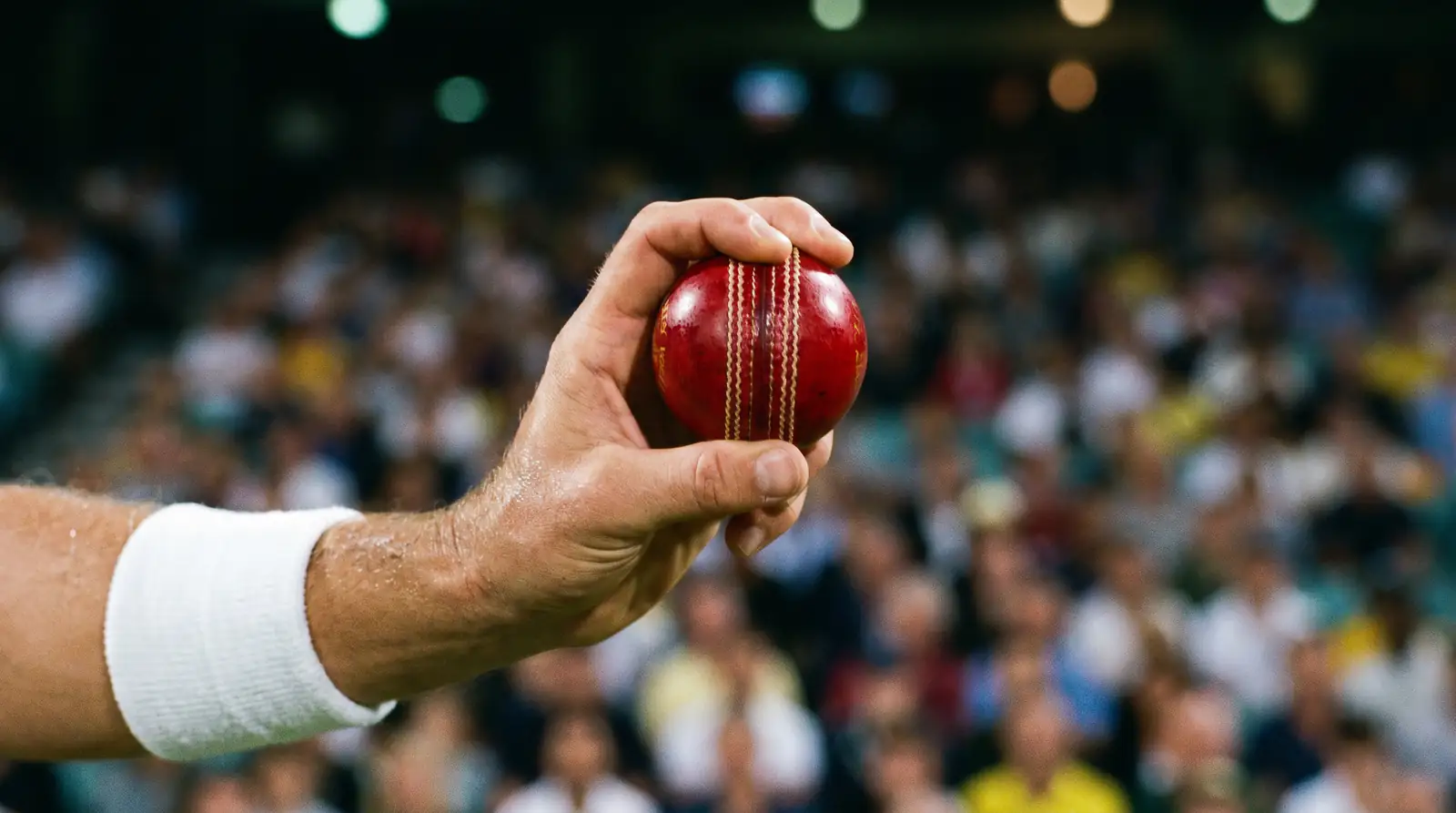 Cricket bowler releasing the ball mid-delivery stride with a packed stadium in the background