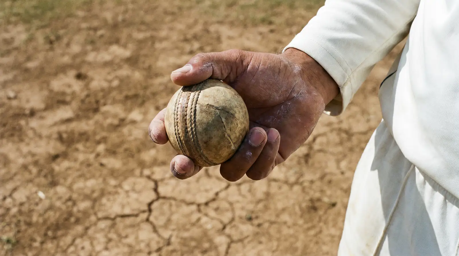 Spin bowler gripping the ball on a dry subcontinental pitch with visible cracks and rough patches