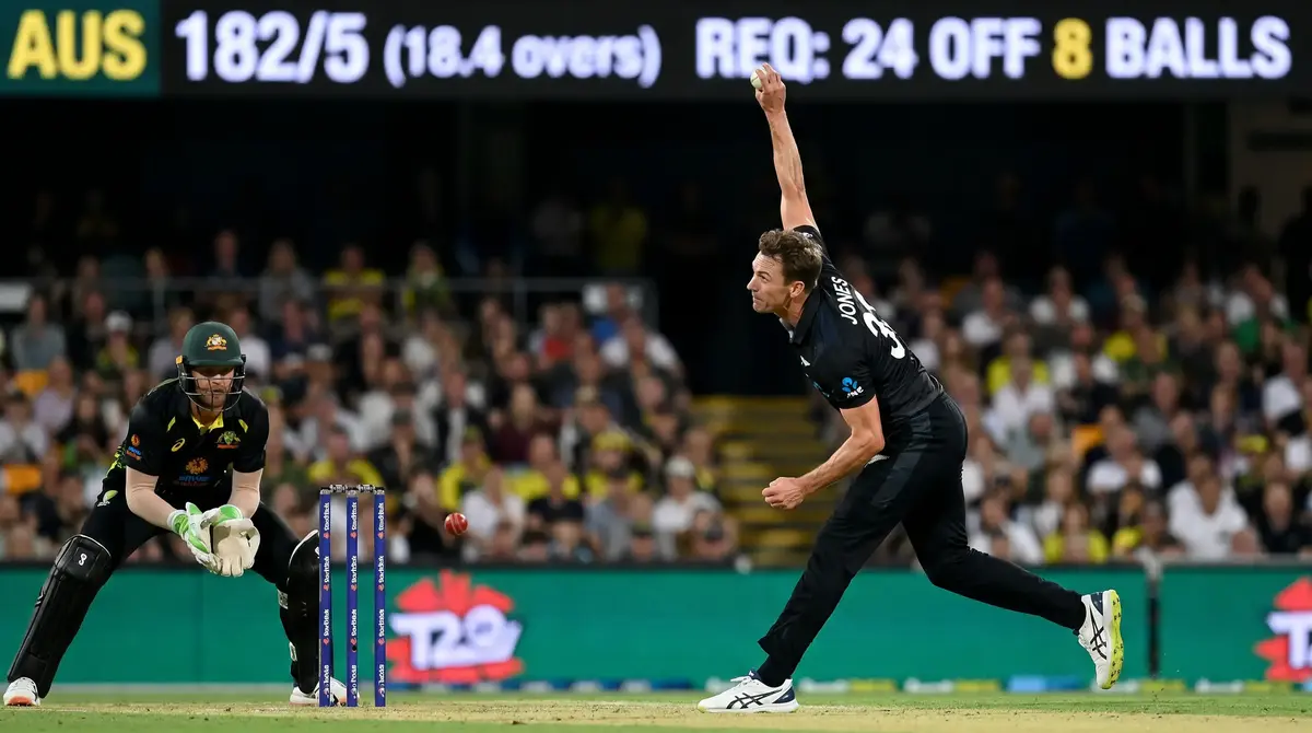 Fast bowler in full delivery stride during a T20 death over under floodlights