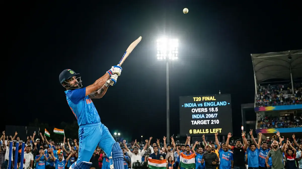 Batsman launching a towering six during T20 death overs with the scoreboard visible behind