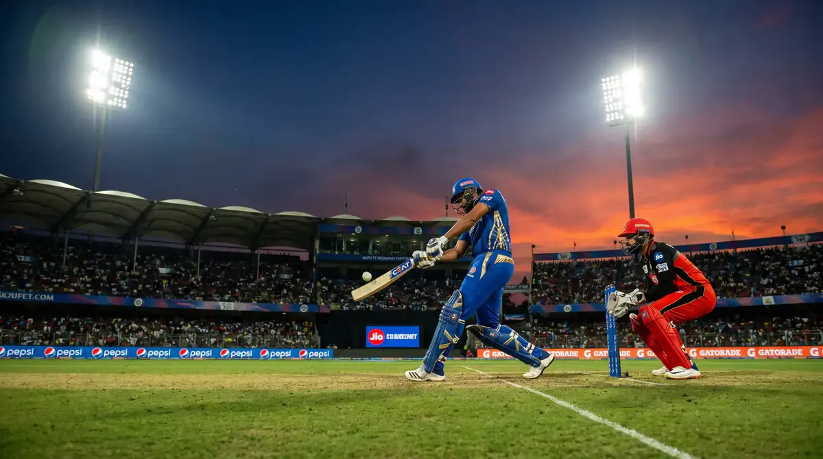 T20 cricket match under floodlights at an evening fixture with colourful team kits