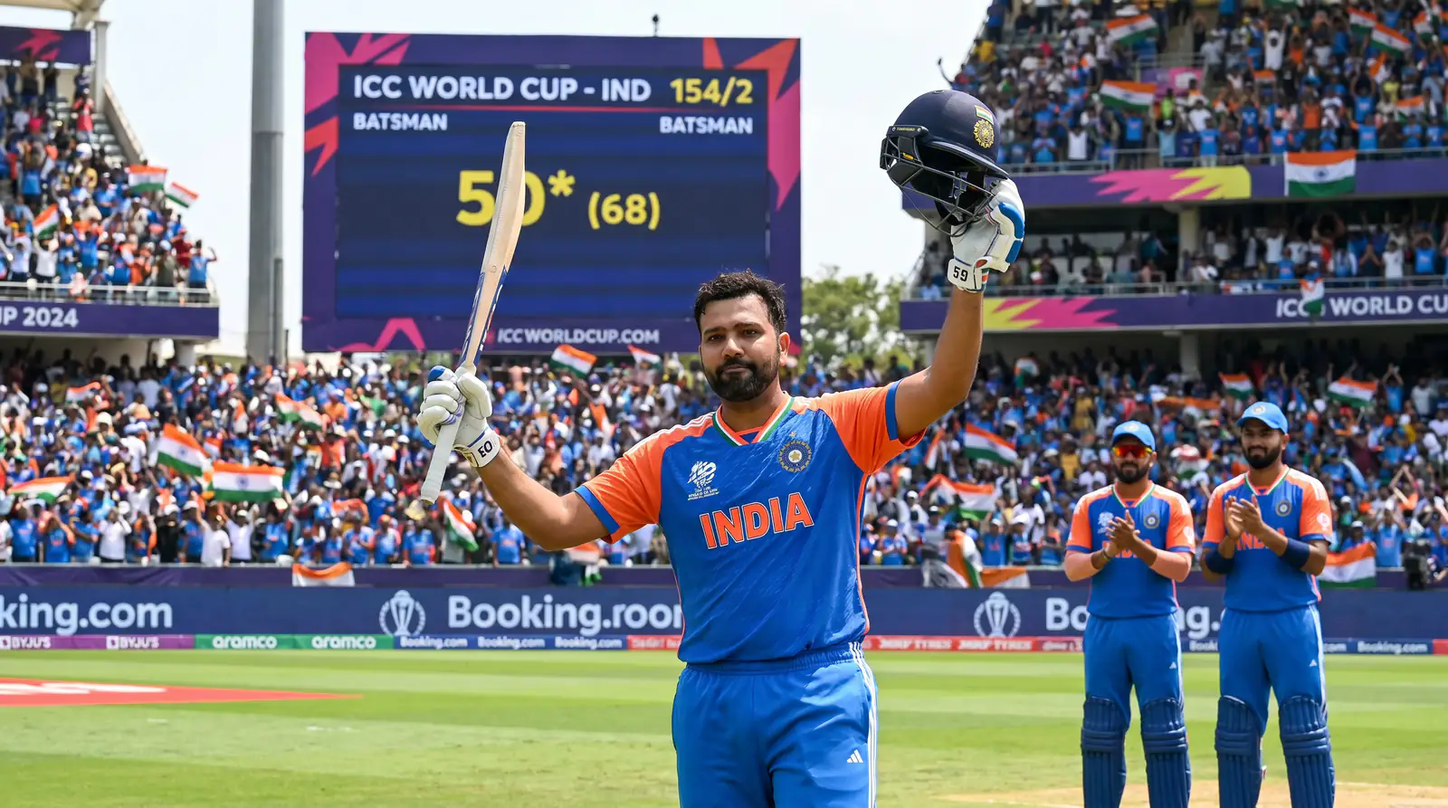Opening batsman raising his bat after reaching fifty in a World Cup match with a large electronic scoreboard behind